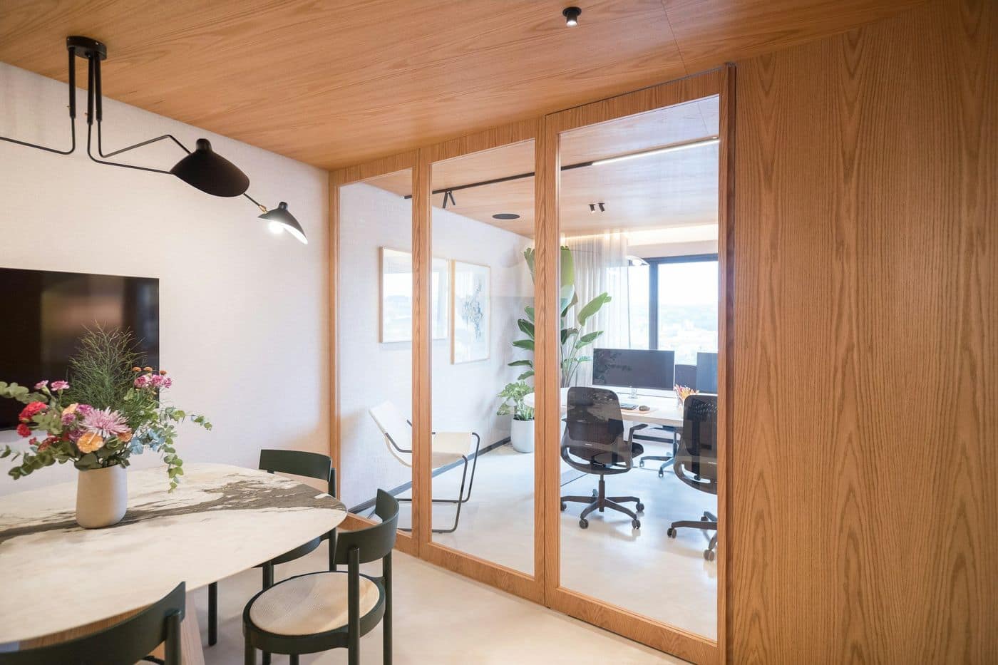 Office with oak-framed glass partitions, white marble meeting table, green chairs and workstations beyond