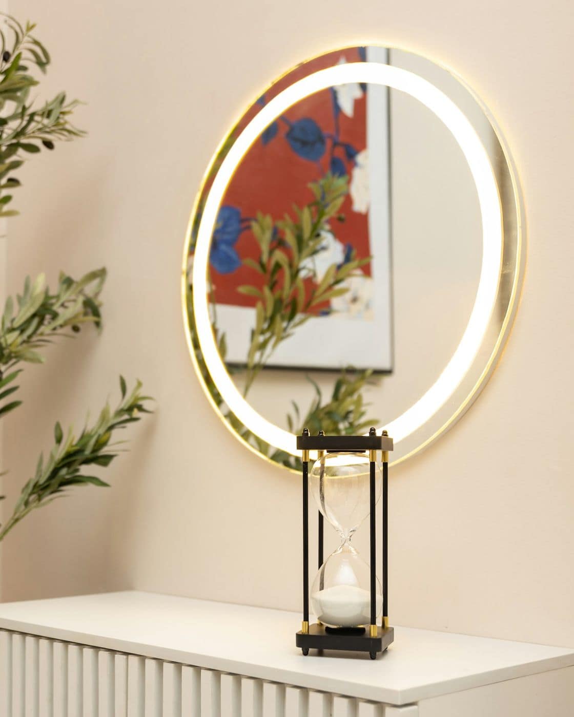 Warm styled corner with backlit round mirror, lantern and olive plant on a fluted white console