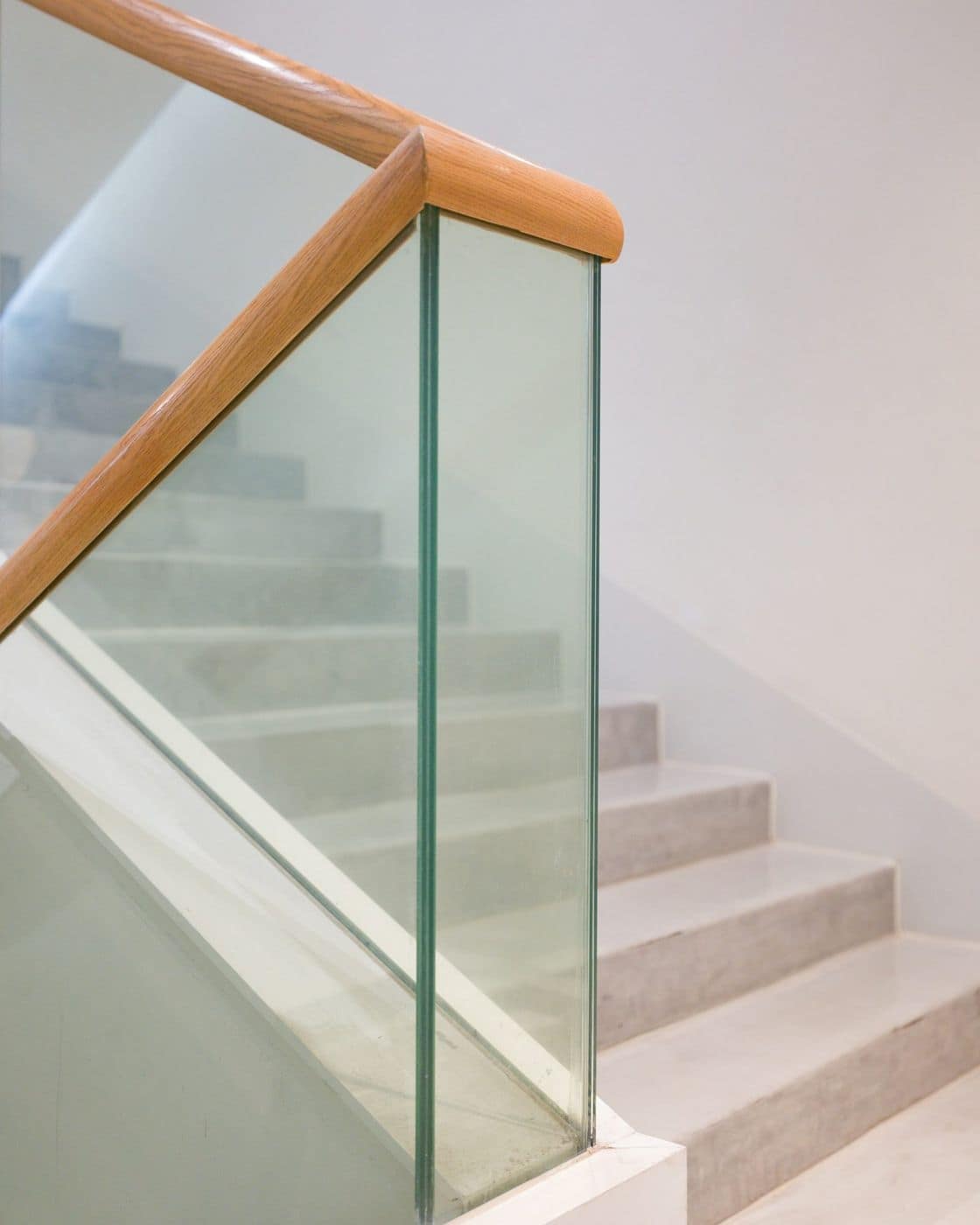 Staircase with marble steps, frameless glass balustrade and wooden handrail against white walls