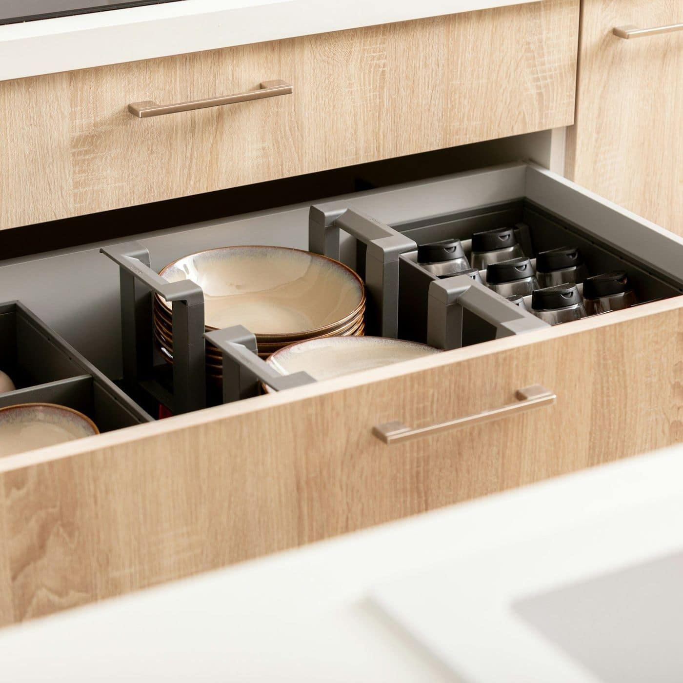 Open oak-finish kitchen drawer with dark organiser holding plates and bowls, slim metal handles
