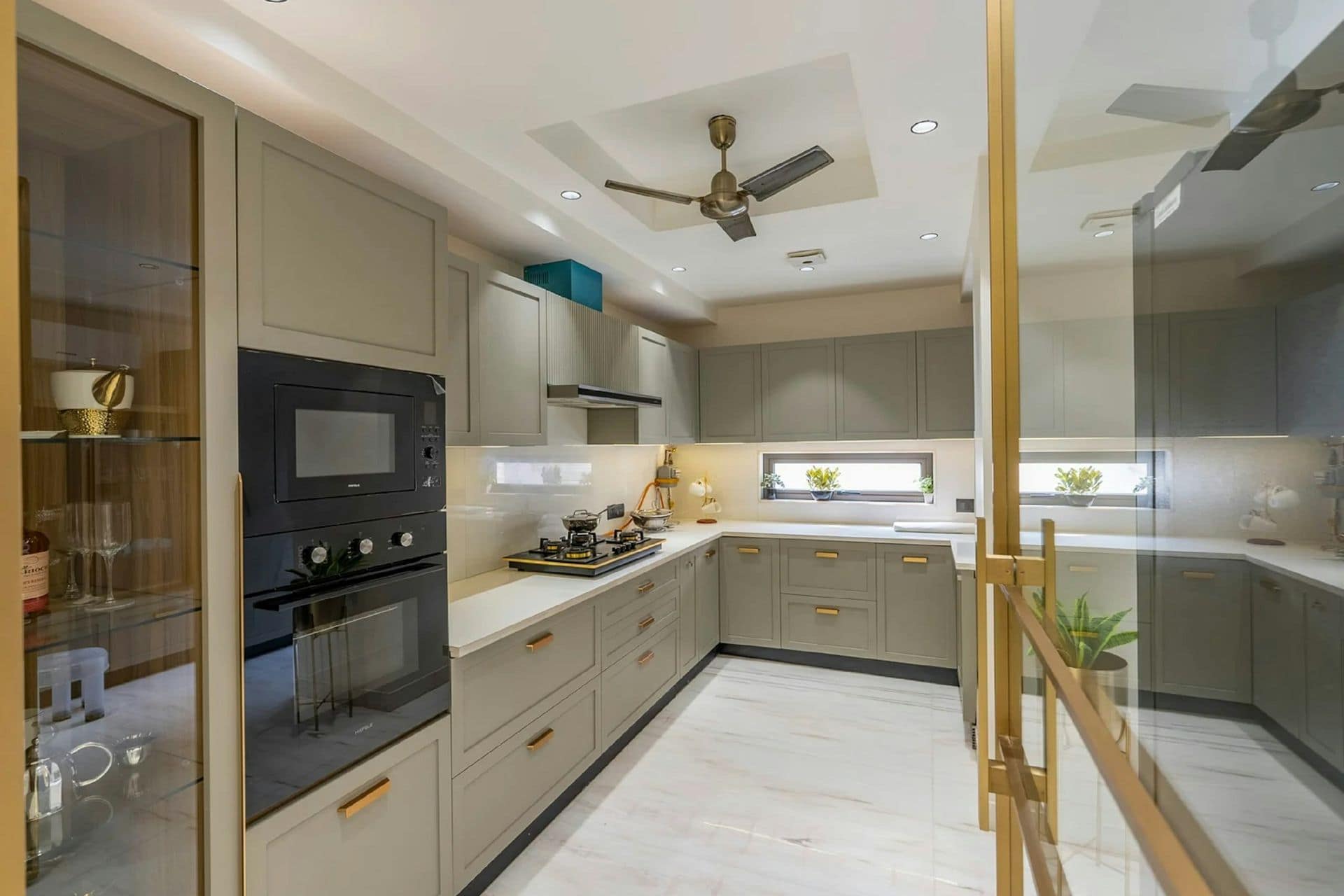 U-shaped modular kitchen with grey laminate shutters, gold handles, built-in oven, quartz counters and ceiling fan