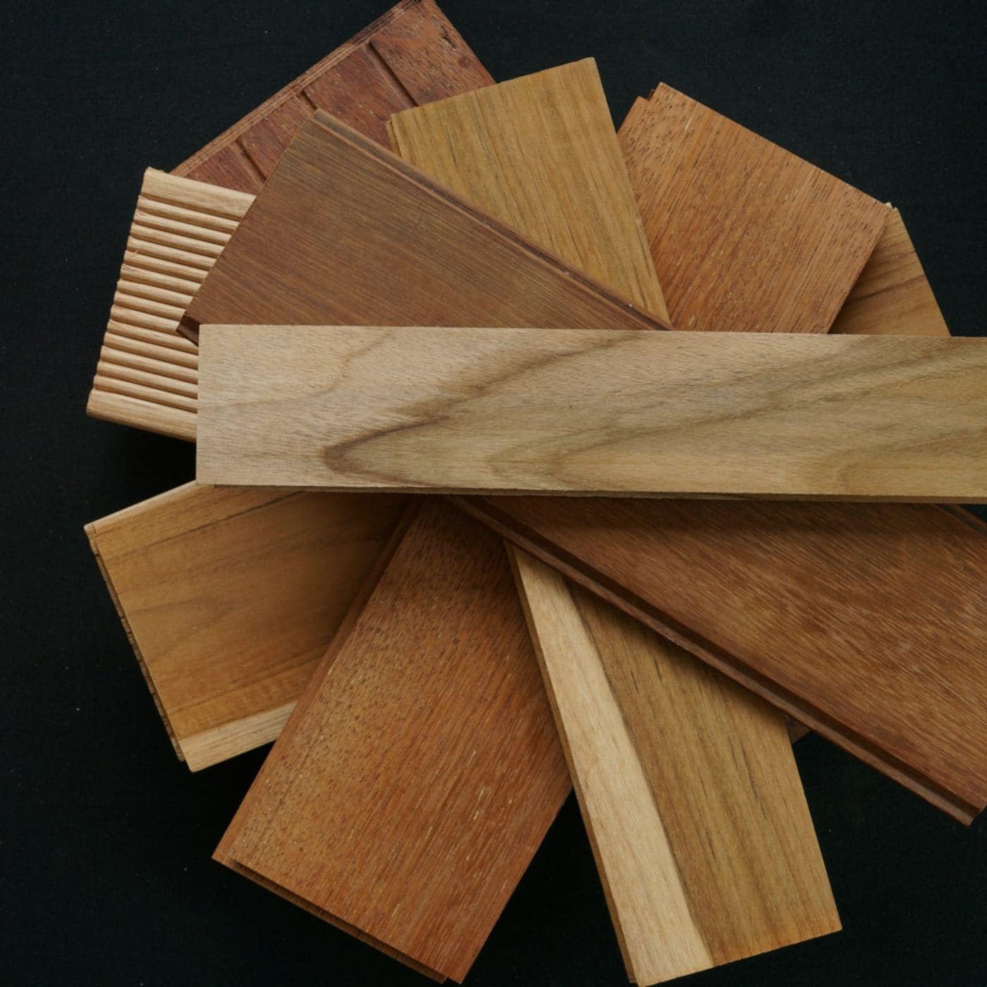 Fan of natural wood plank samples in oak, teak and walnut tones on a black background