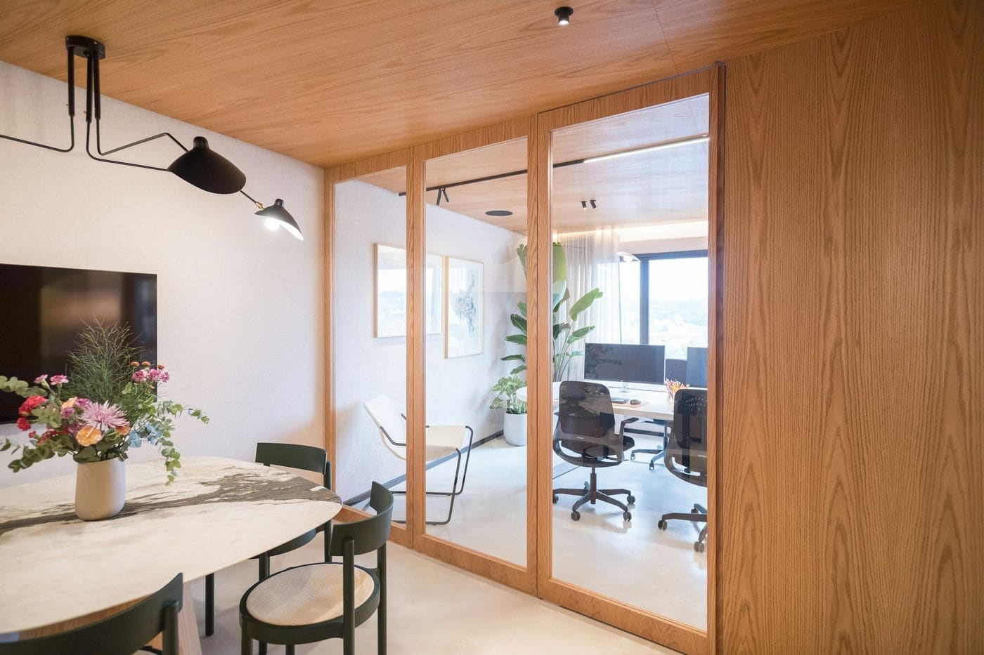 Office with oak-framed glass partitions, white marble meeting table, green chairs and workstations beyond
