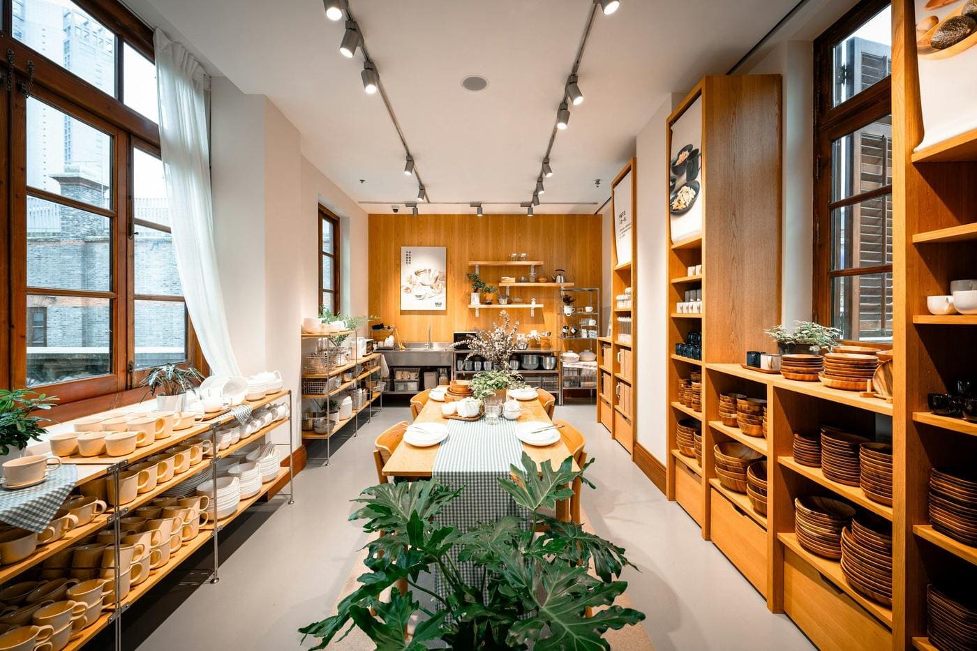 Homeware store with tall oak shelving of ceramics and wooden plates, track lights and long display table