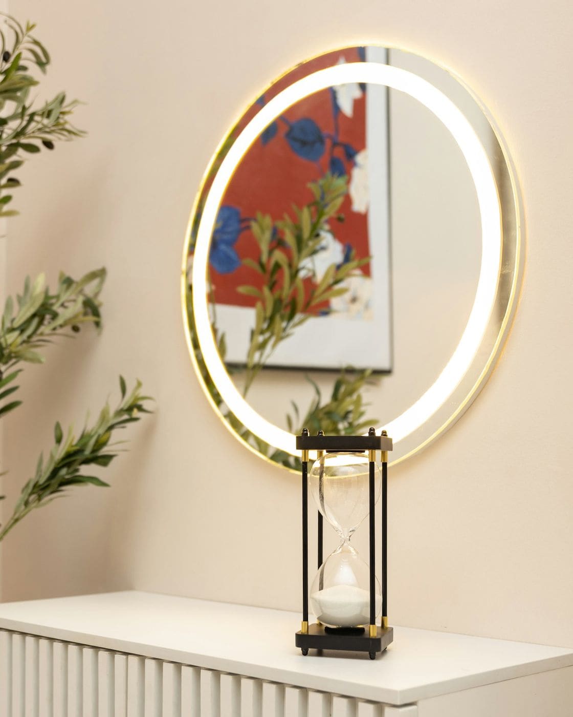 Warm styled corner with backlit round mirror, lantern and olive plant on a fluted white console